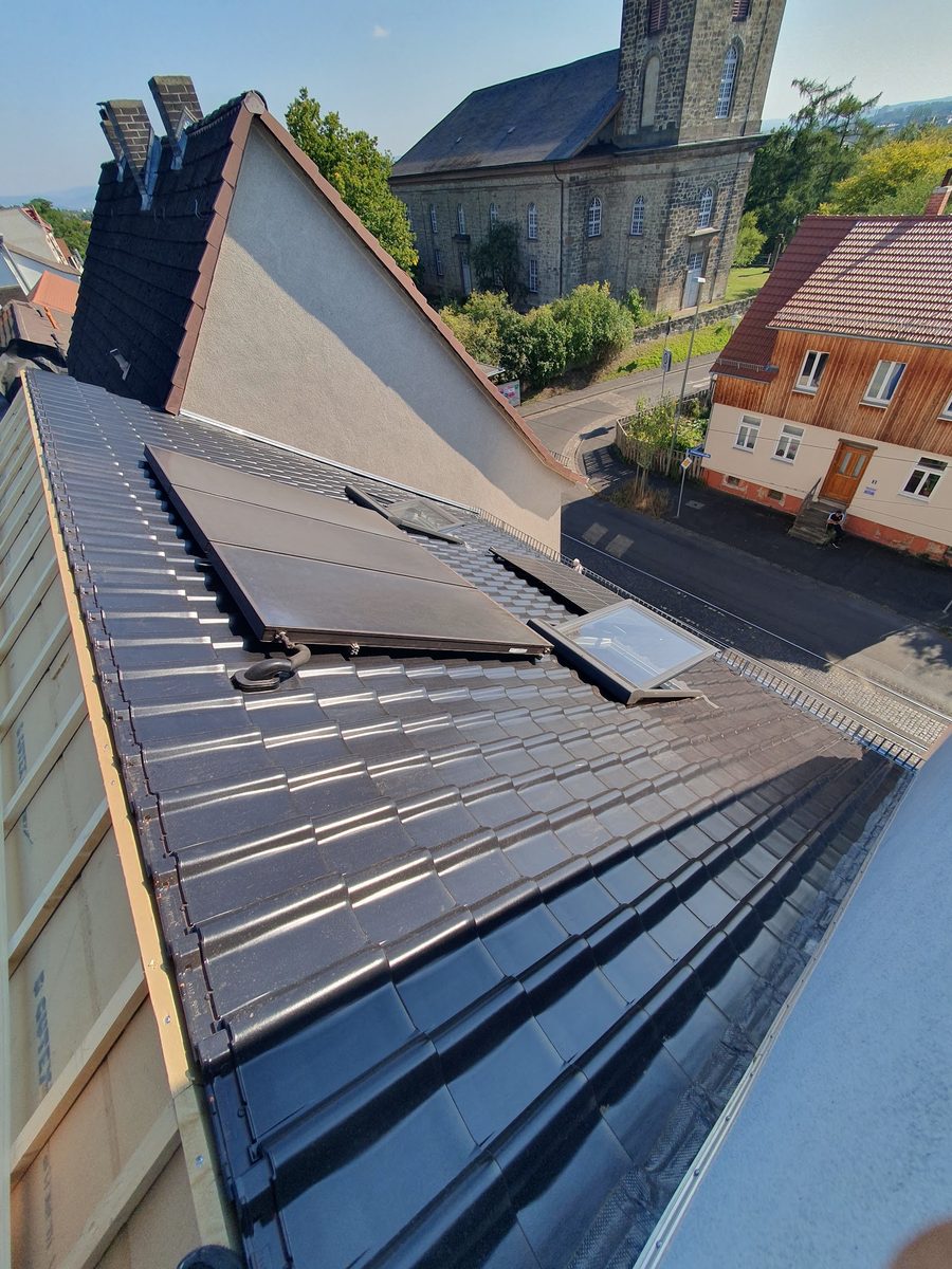 Dach mit Dachfenster und Solarmodulen vor einer Kirche